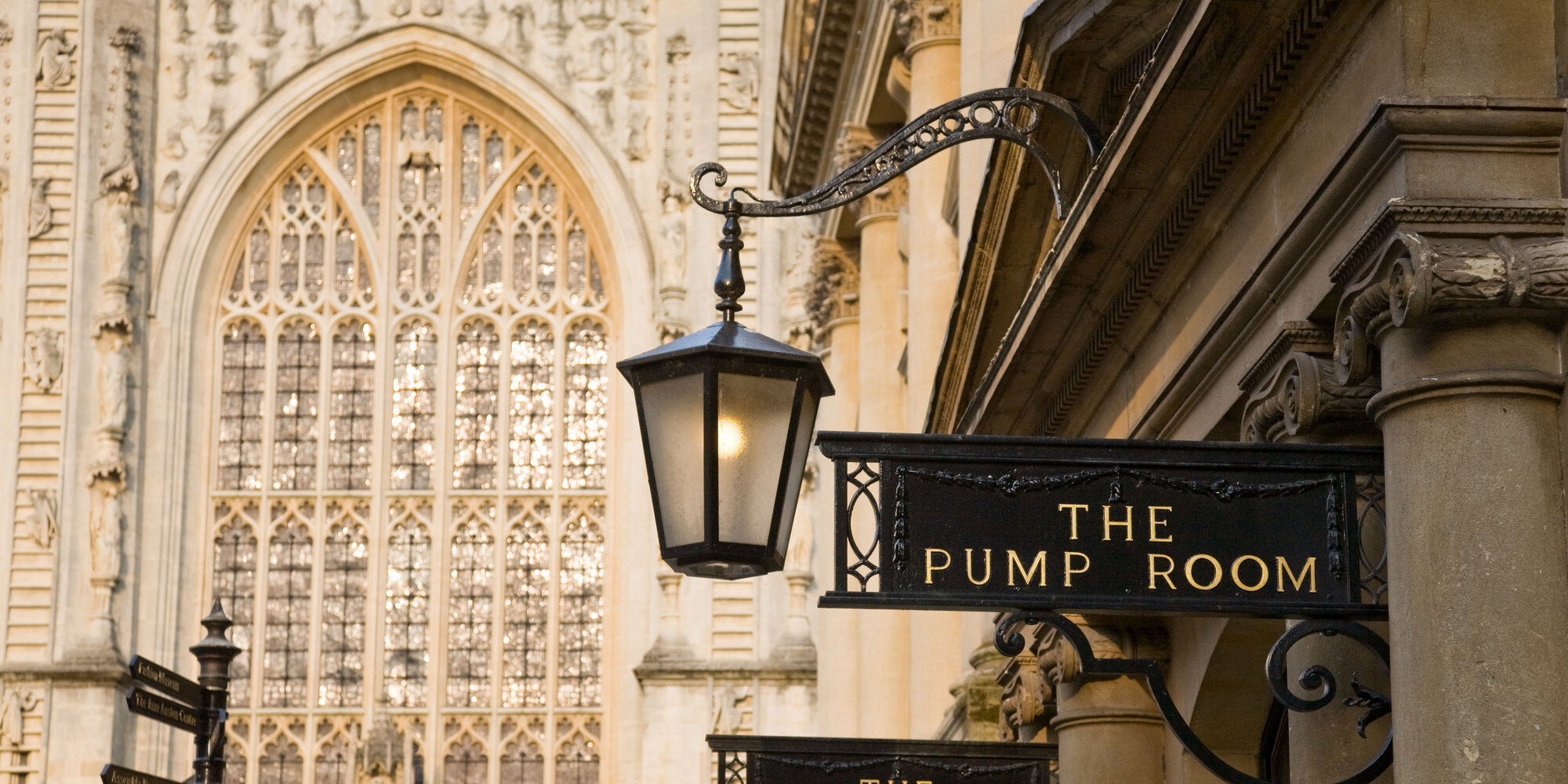 DC97JT Bath Pump rooms exterior signs and columns with the west window of Bath Abbey in the background.